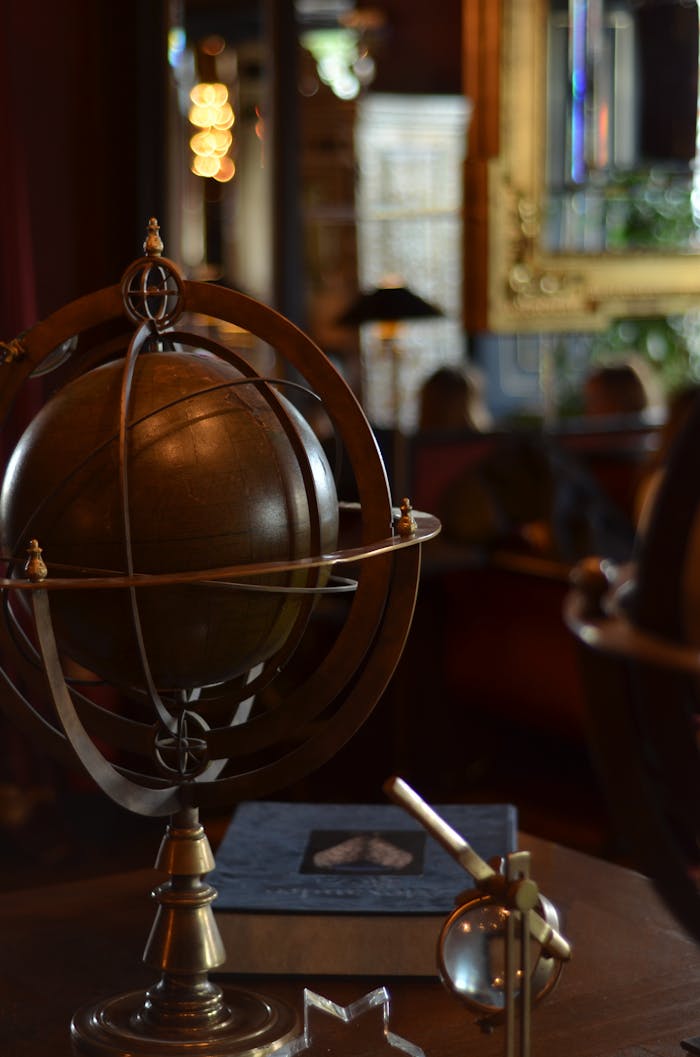 A vintage brass globe on a wooden table in a warmly lit interior, with classic decor elements.